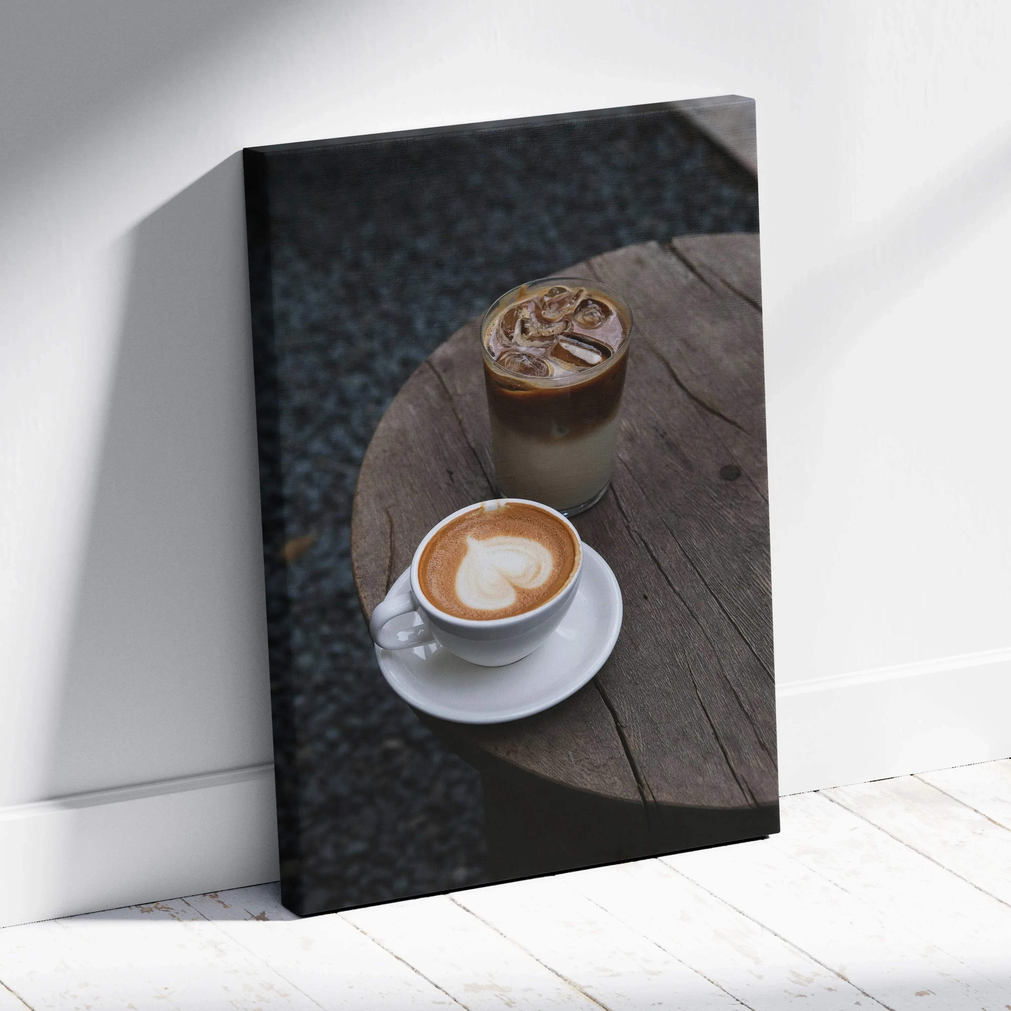 A framed canvas print showing two coffee drinks with latte art and iced coffee on a rustic wooden table in warm tones