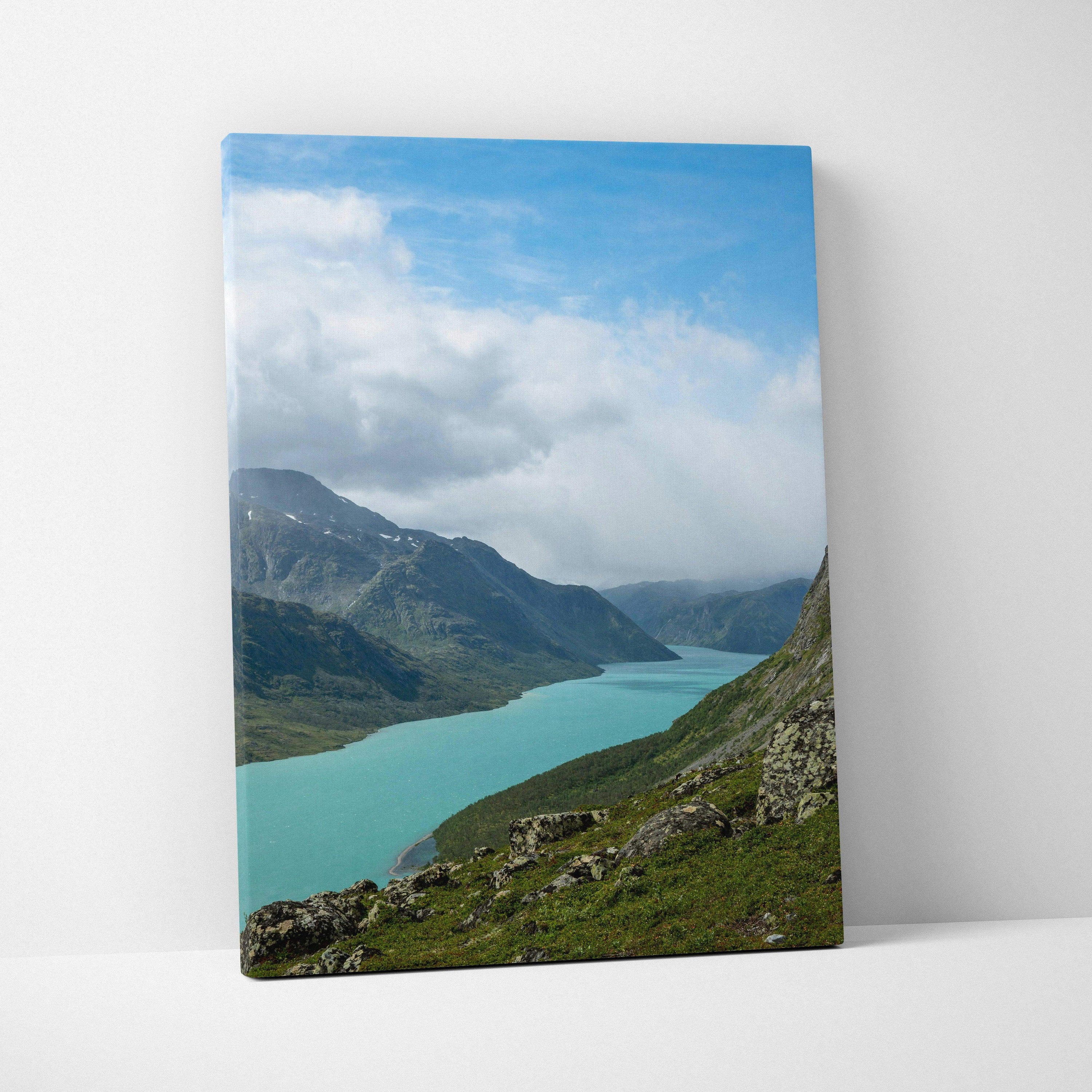 Vertical canvas wall art featuring a turquoise mountain lake under a partly cloudy blue sky.