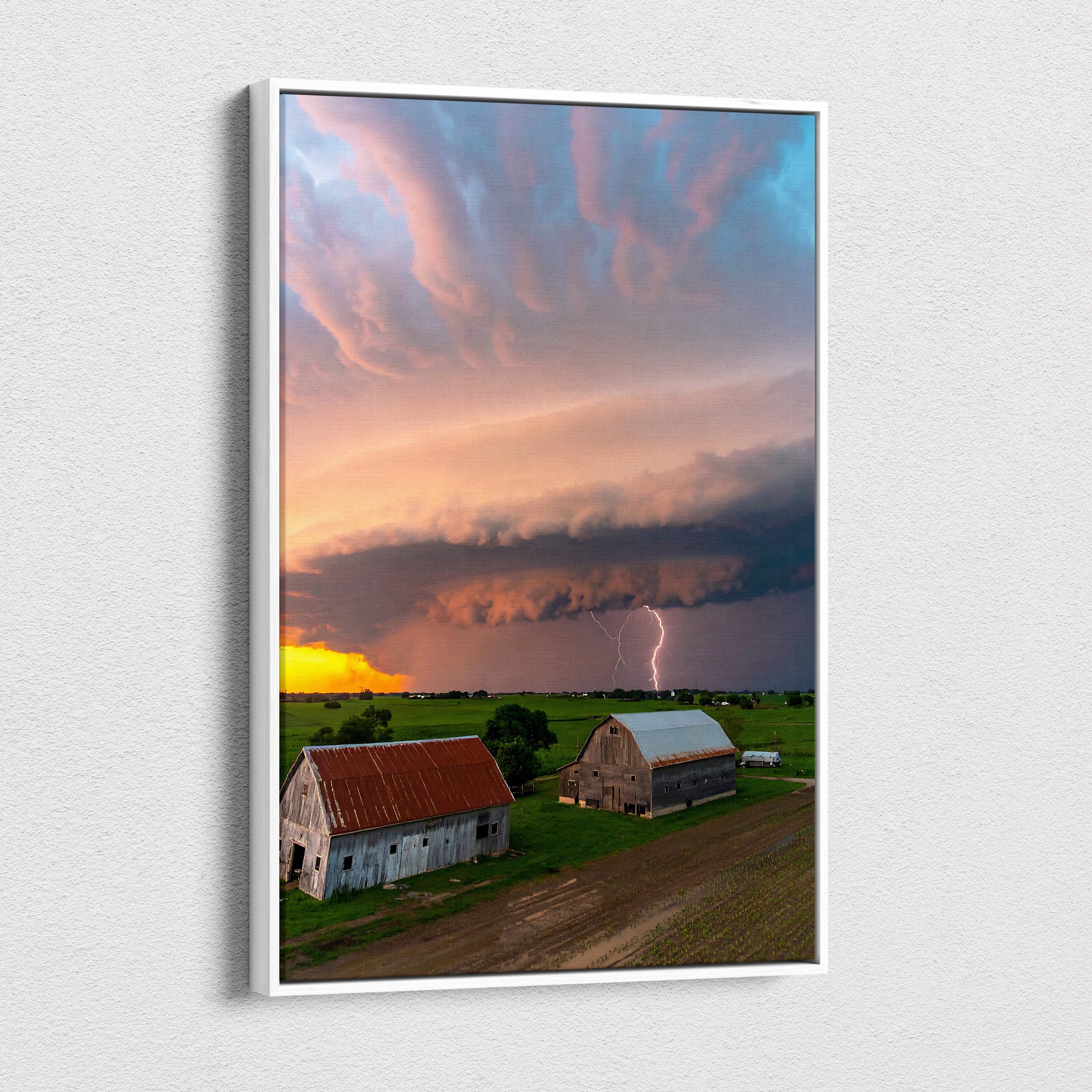 A framed canvas print of a dramatic rural landscape with barns under lightning and vibrant pink orange blue clouds