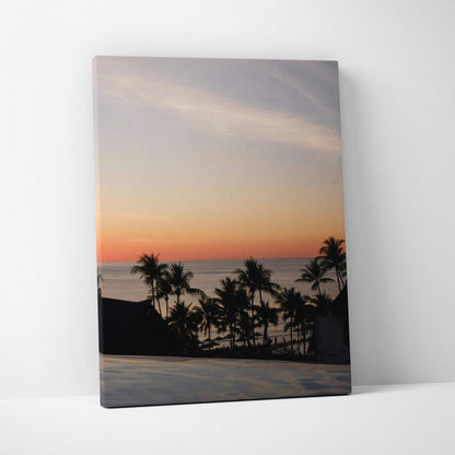 Canvas wall art featuring a vivid golden sunset over a beach with silhouetted palm trees and calm ocean.