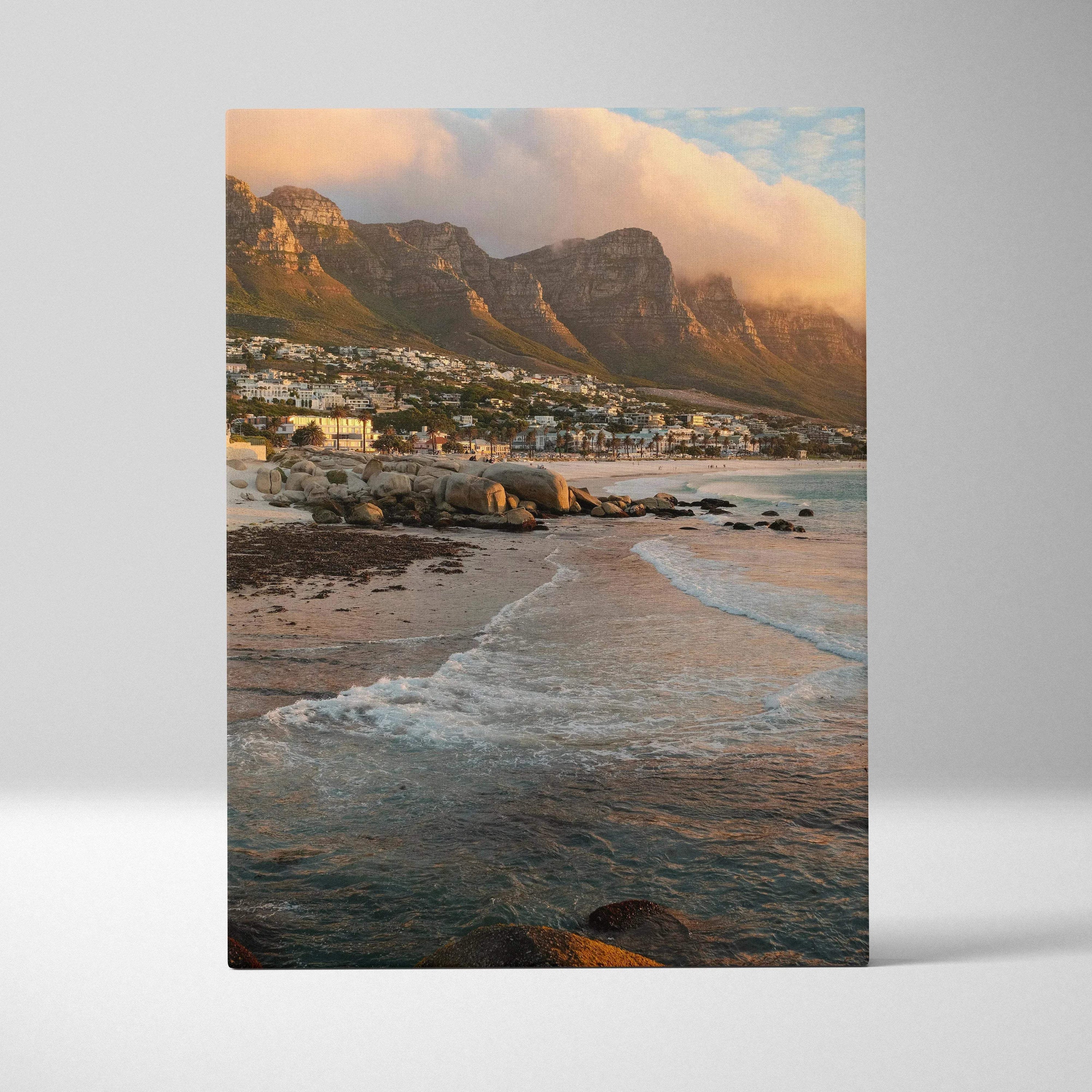 Canvas wall art featuring golden-lit mountains overlooking a rocky beach with gentle waves.