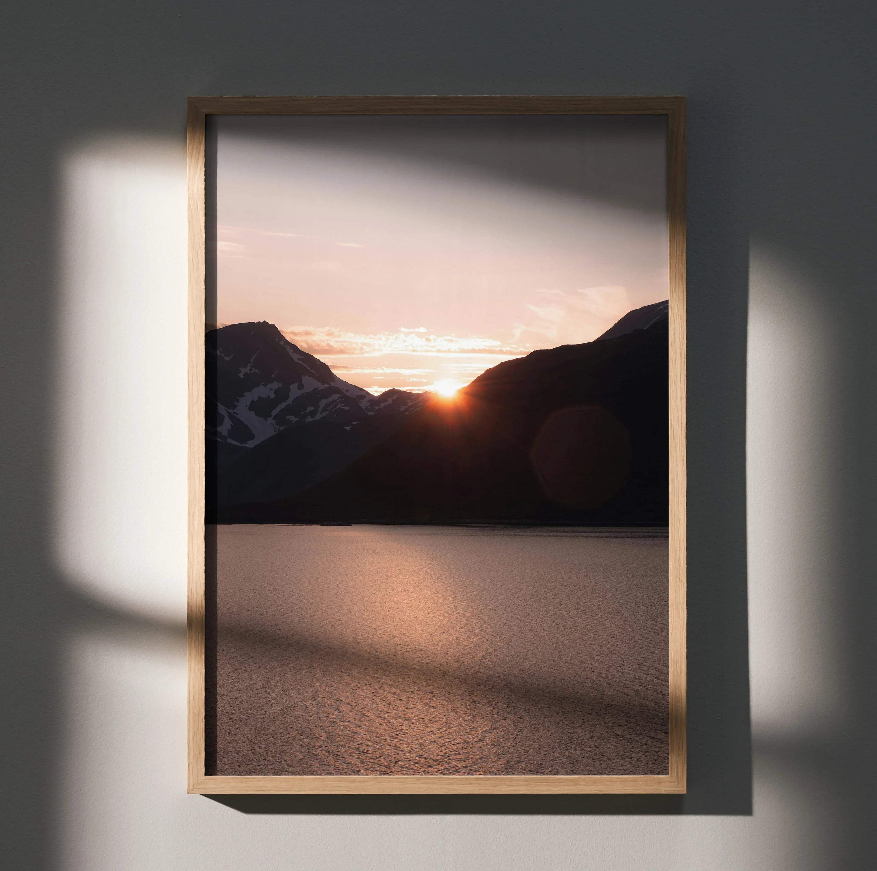 Vertical wall art poster of a sunset behind dark mountain silhouettes over calm water.