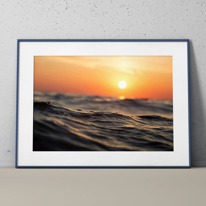 Serene ocean sunset poster wall art with warm orange and blue tones in a black frame.