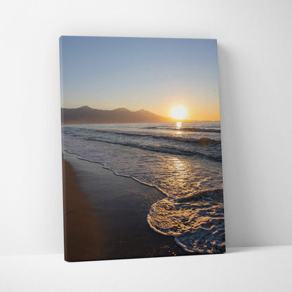 Canvas wall art featuring a sunset over ocean waves with distant mountains and sandy shore.