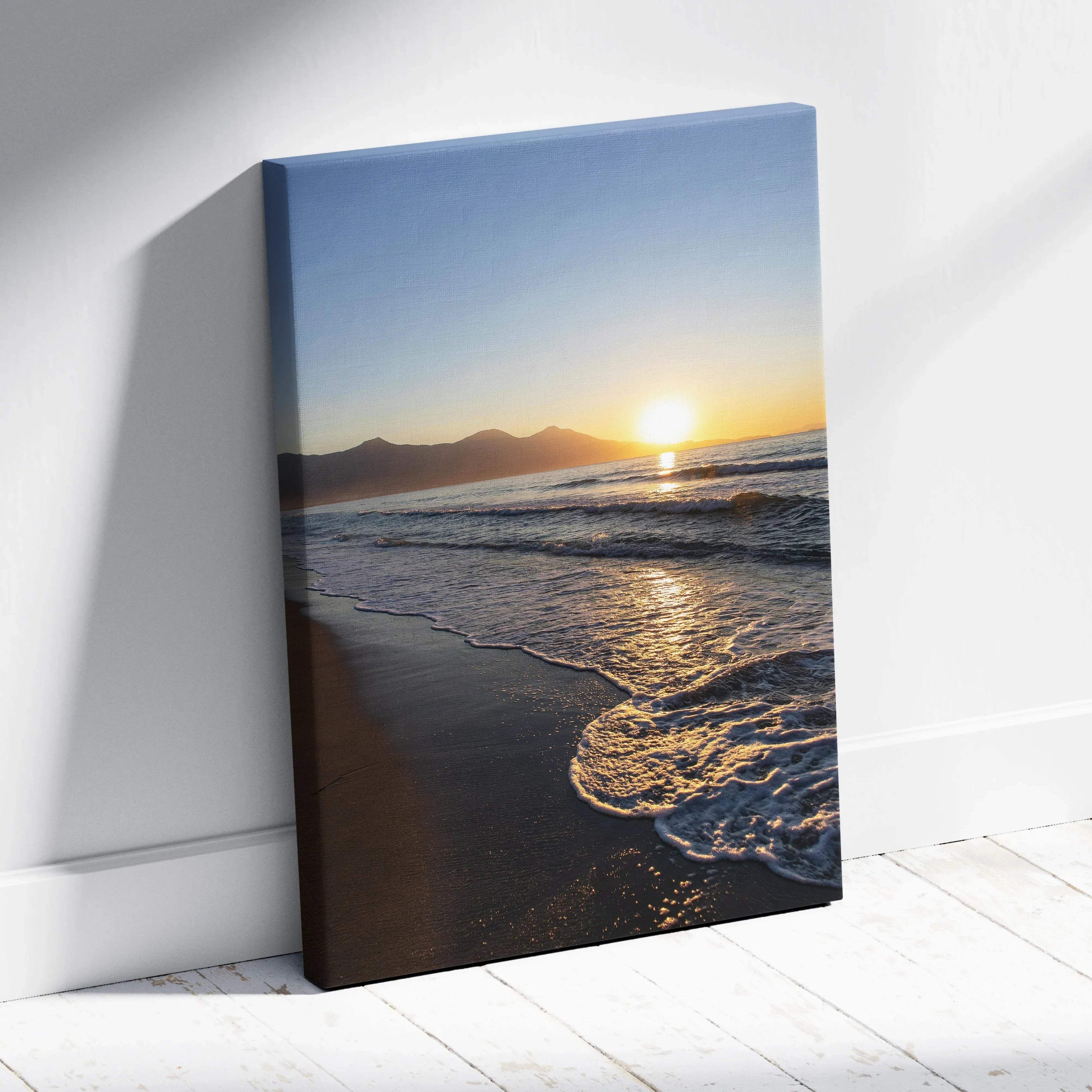 Canvas wall art featuring a sunset over mountains and ocean waves on a sandy beach.