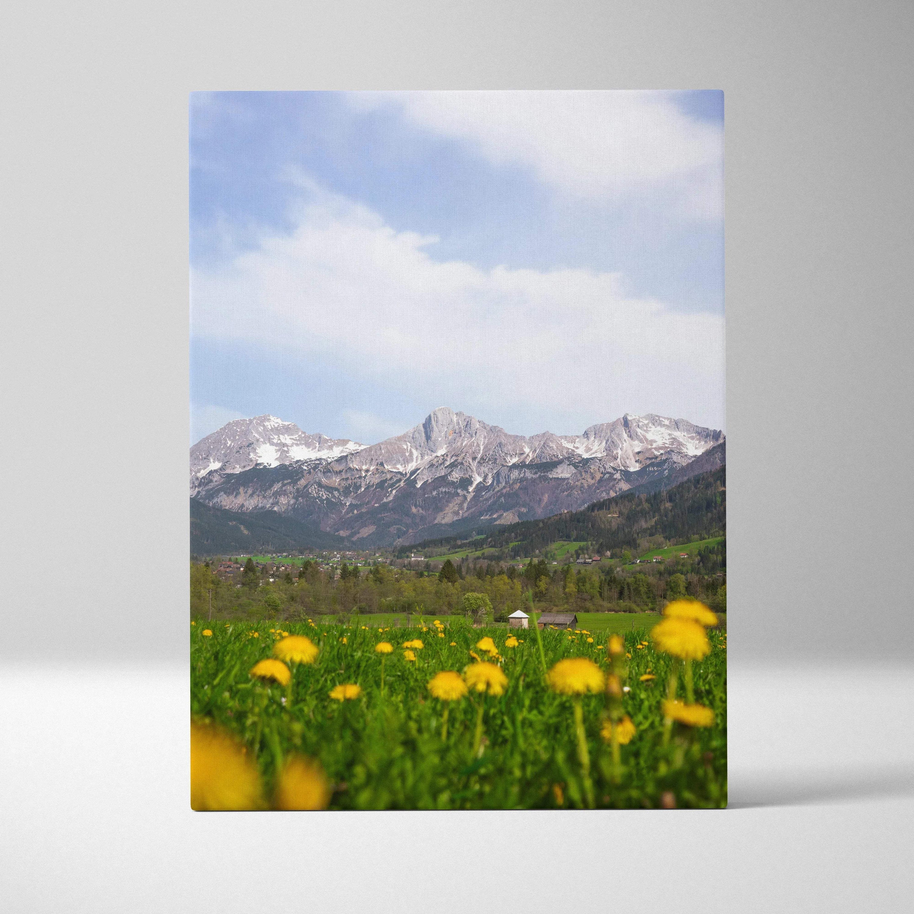 Vertical canvas wall art depicting snow-capped mountains and green meadow with yellow wildflowers under a blue sky.