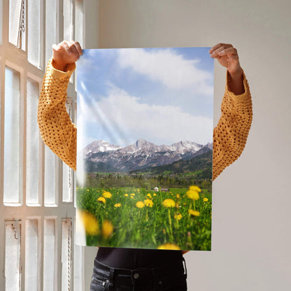 Vertical wall art poster featuring majestic snow-capped mountains with a green meadow and yellow flowers under a blue sky.