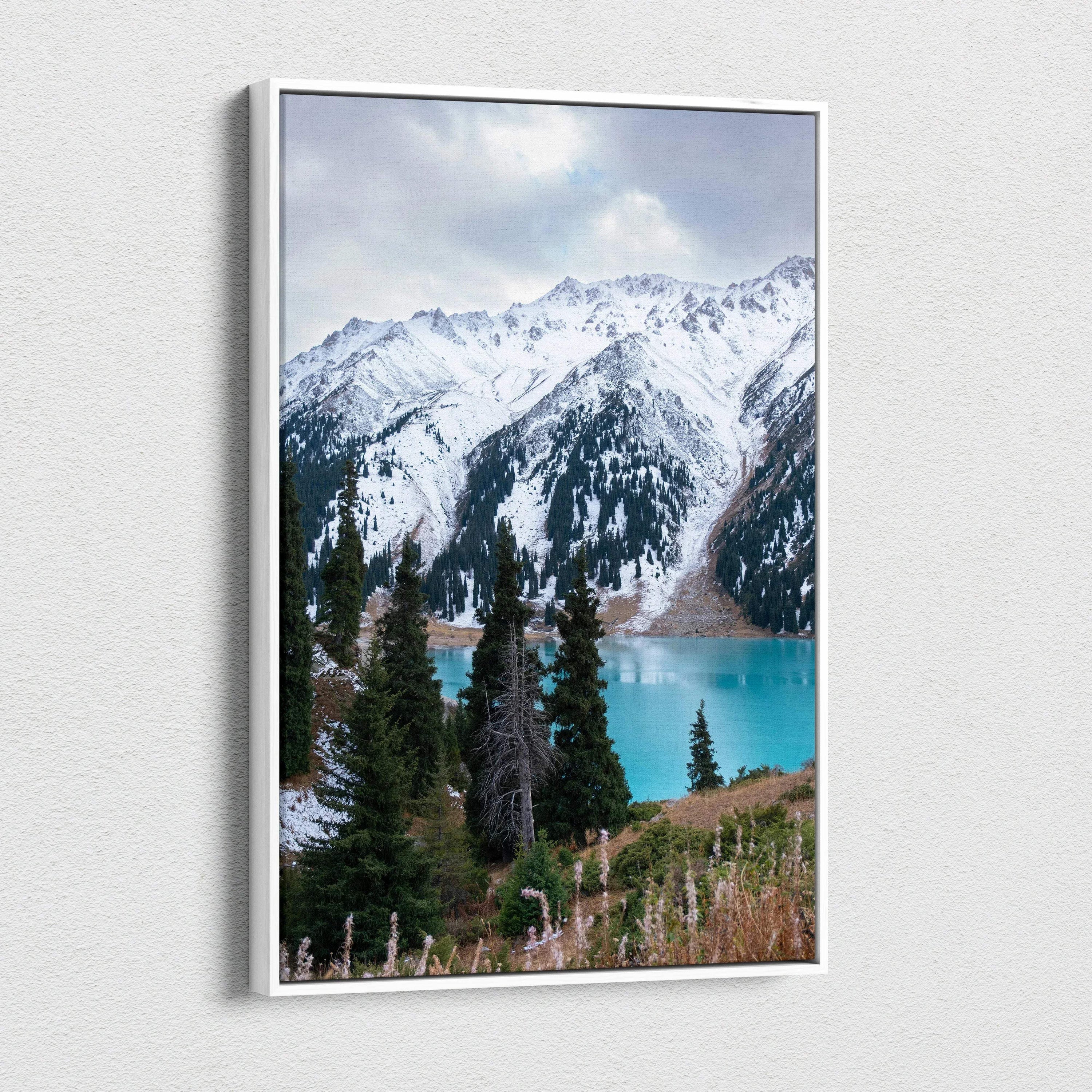Vertical canvas wall art featuring snow-capped mountains with pine trees and a turquoise lake.