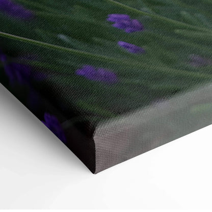 Close-up of vibrant floral canvas wall art with purple flowers and green leaves on textured canvas.