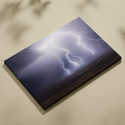 A rectangular canvas print of bright white lightning bolts against a dark moody stormy sky and mountain landscape wall decor