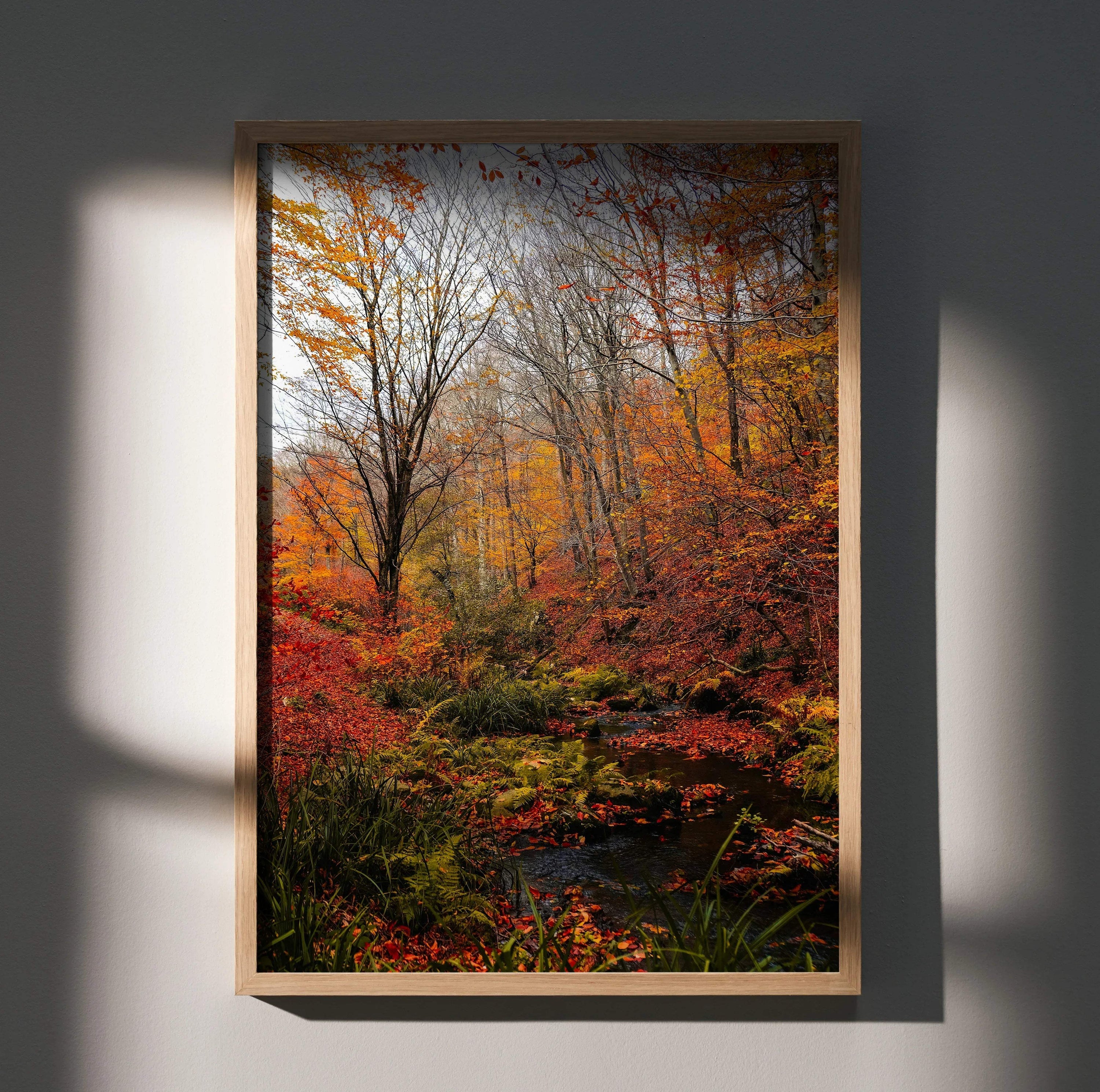 Vertical autumn forest wall art poster with vibrant orange and red foliage and a small stream.