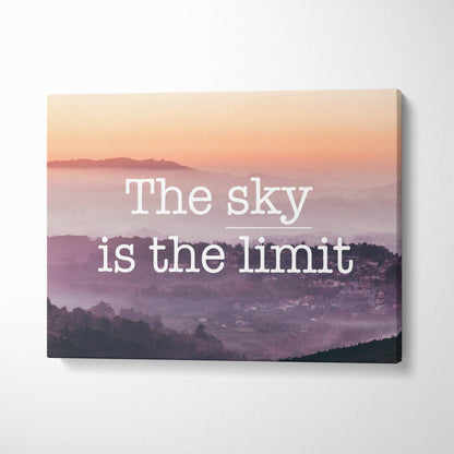 A rectangular canvas print of a misty mountain sunrise with pink and purple hues featuring the sky is the limit text