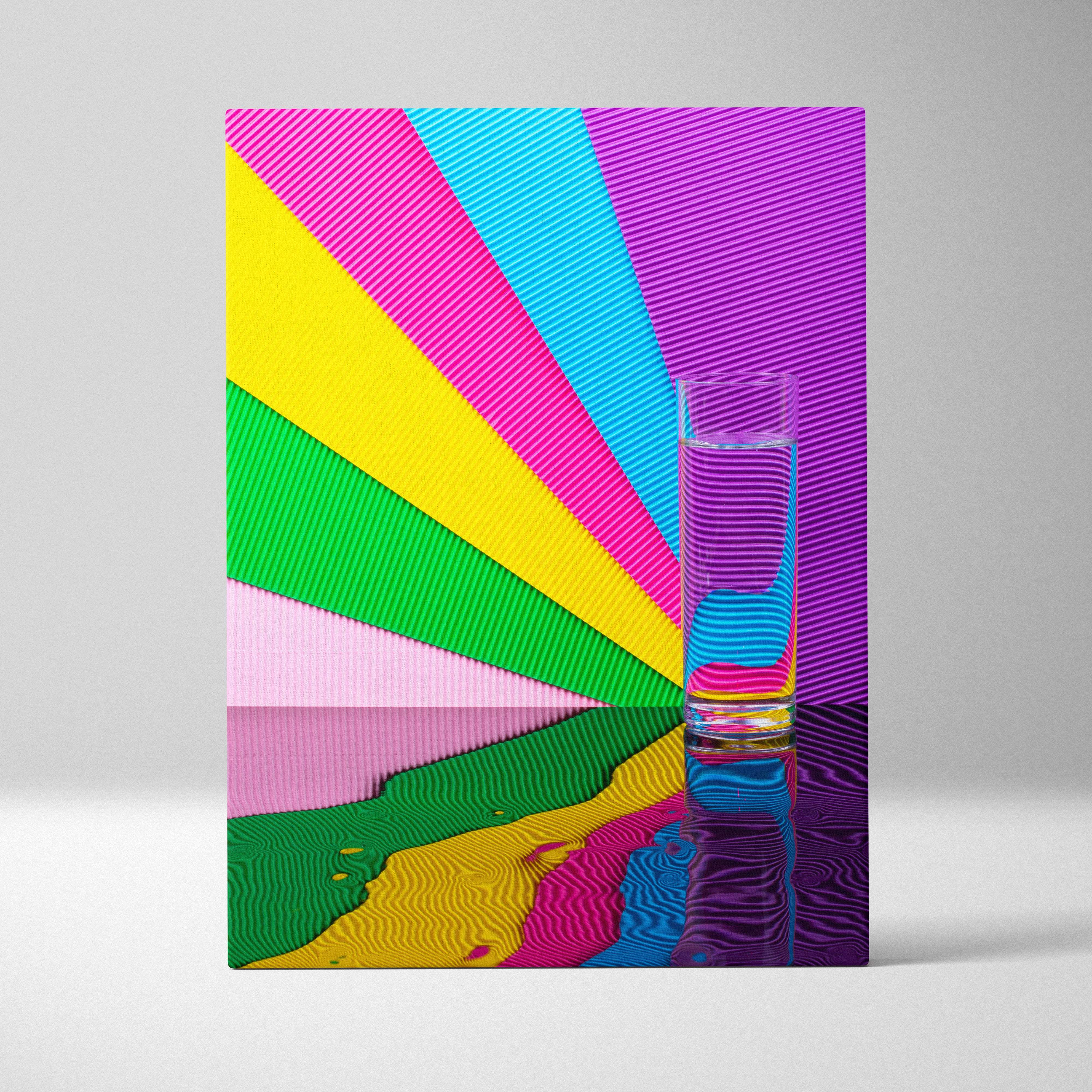 A clear glass tumbler filled with water on a reflective surface against a vibrant rainbow striped contemporary wall art