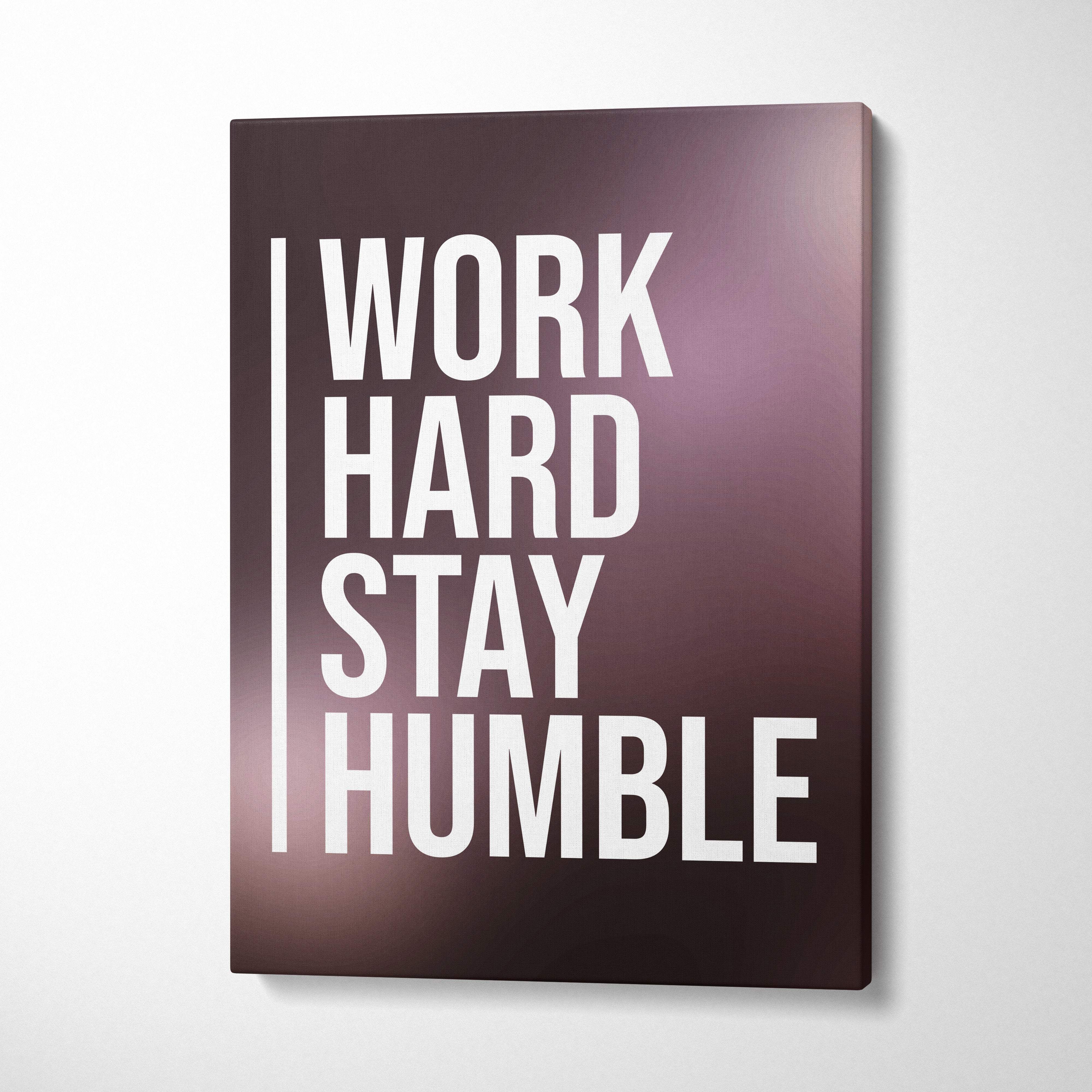 A rectangular canvas print with bold white work hard stay humble text on a gradient dark purple background for office decor