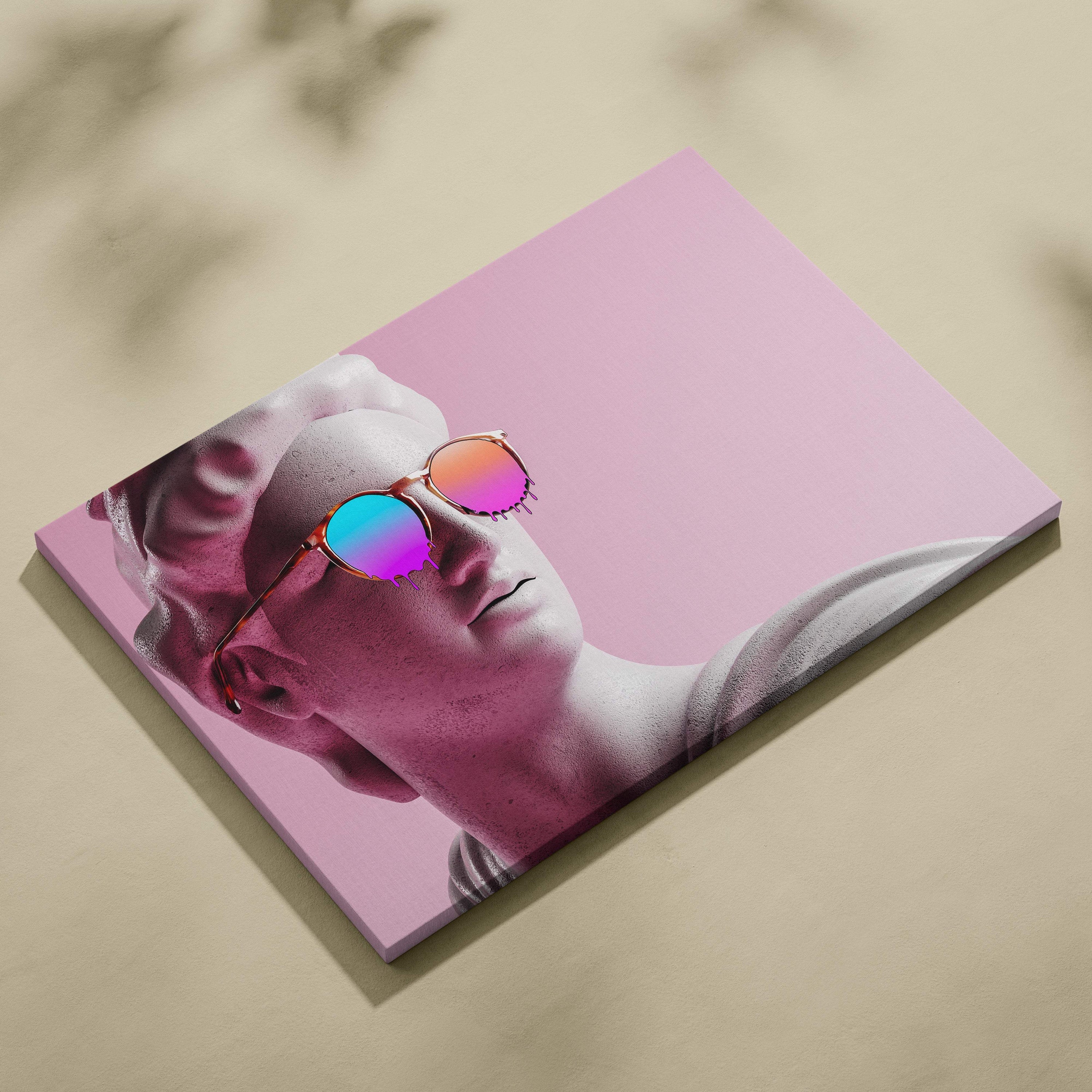 A rectangular canvas print featuring a classical statue’s face wearing vibrant, iridescent sunglasses against a solid pink background.