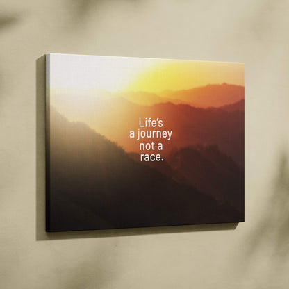 A rectangular canvas print featuring a warm orange mountain sunset with lifes a journey not a race quote mounted on a wall