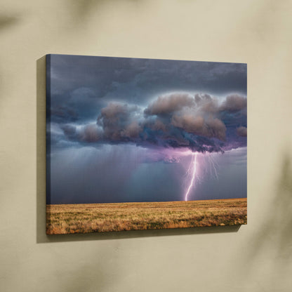 Canvas print of a dramatic thunderstorm over a prairie with moody blue clouds and a vivid purple lightning strike