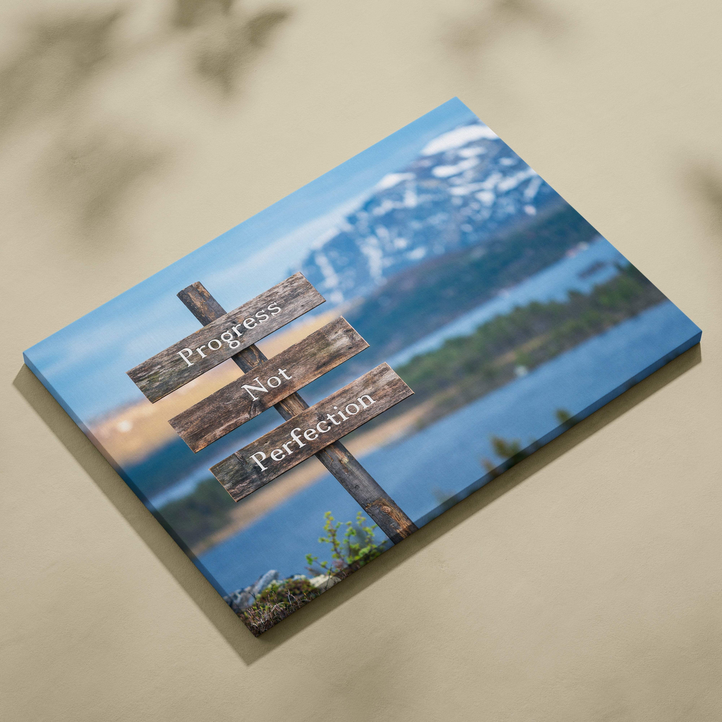 Motivational progress not perfection canvas wall art featuring rustic dark brown wooden sign with white text and mountain lake backdrop
