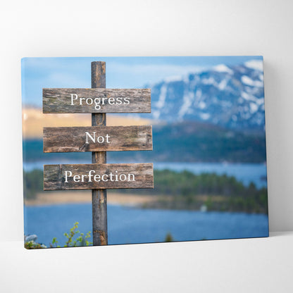 Rustic wooden canvas wall art with progress not perfection quote on weathered planks against blue lake mountain backdrop