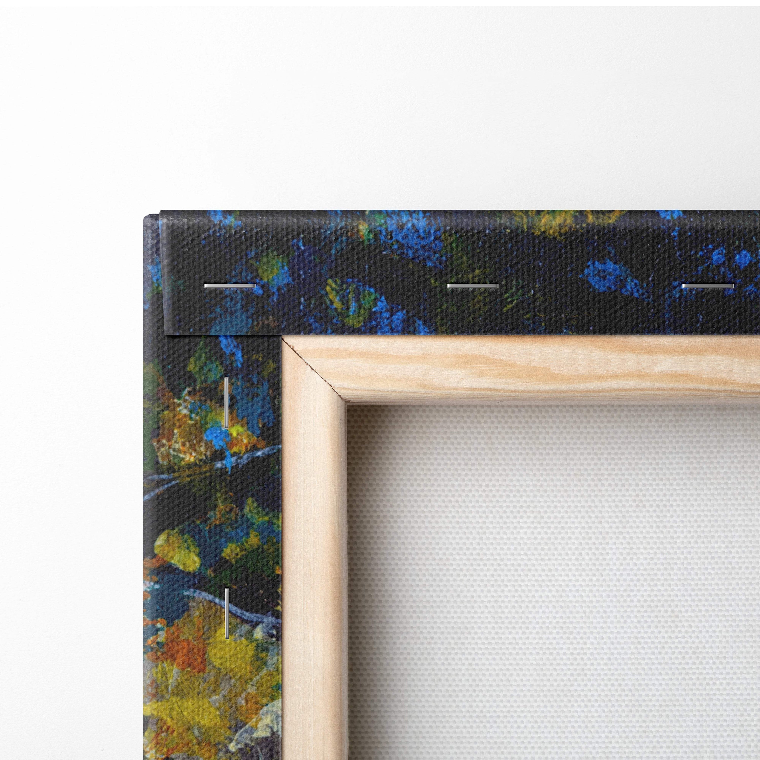 Light-colored wooden frame holding sunlit forest path canvas print with blue green yellow abstract paint splatters