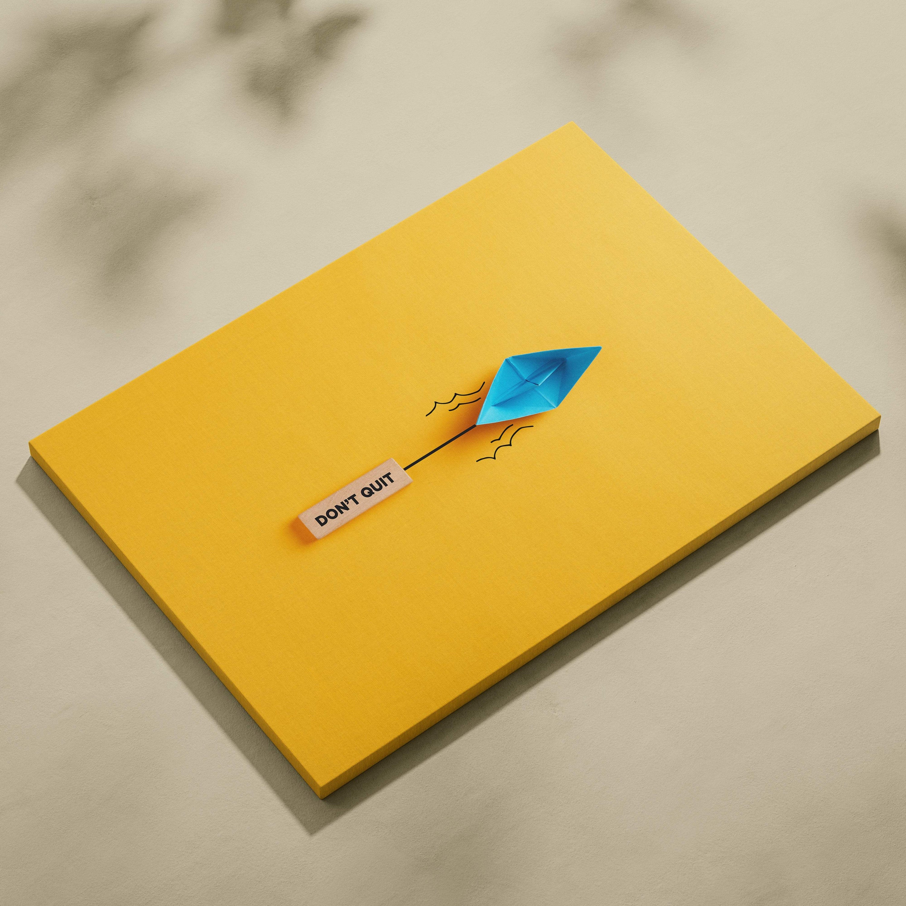 Motivational don’t quit canvas wall art with a yellow notepad and blue origami paper boat featuring an inspirational sticker