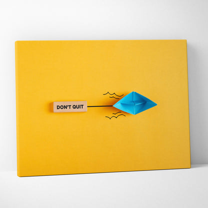 Motivational don’t quit canvas wall art with a blue paper boat black ink waves and wooden plaque on vibrant yellow background