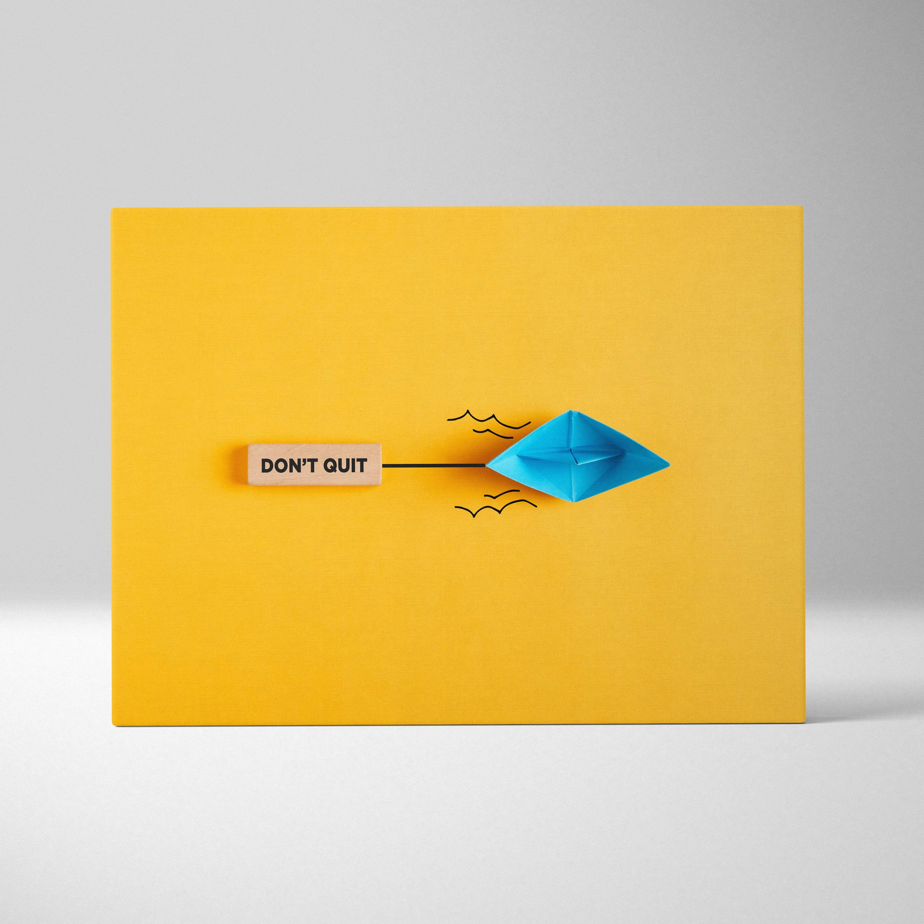 A vibrant blue origami paper boat with crisp folds on a minimalist yellow canvas for positive mindset decor
