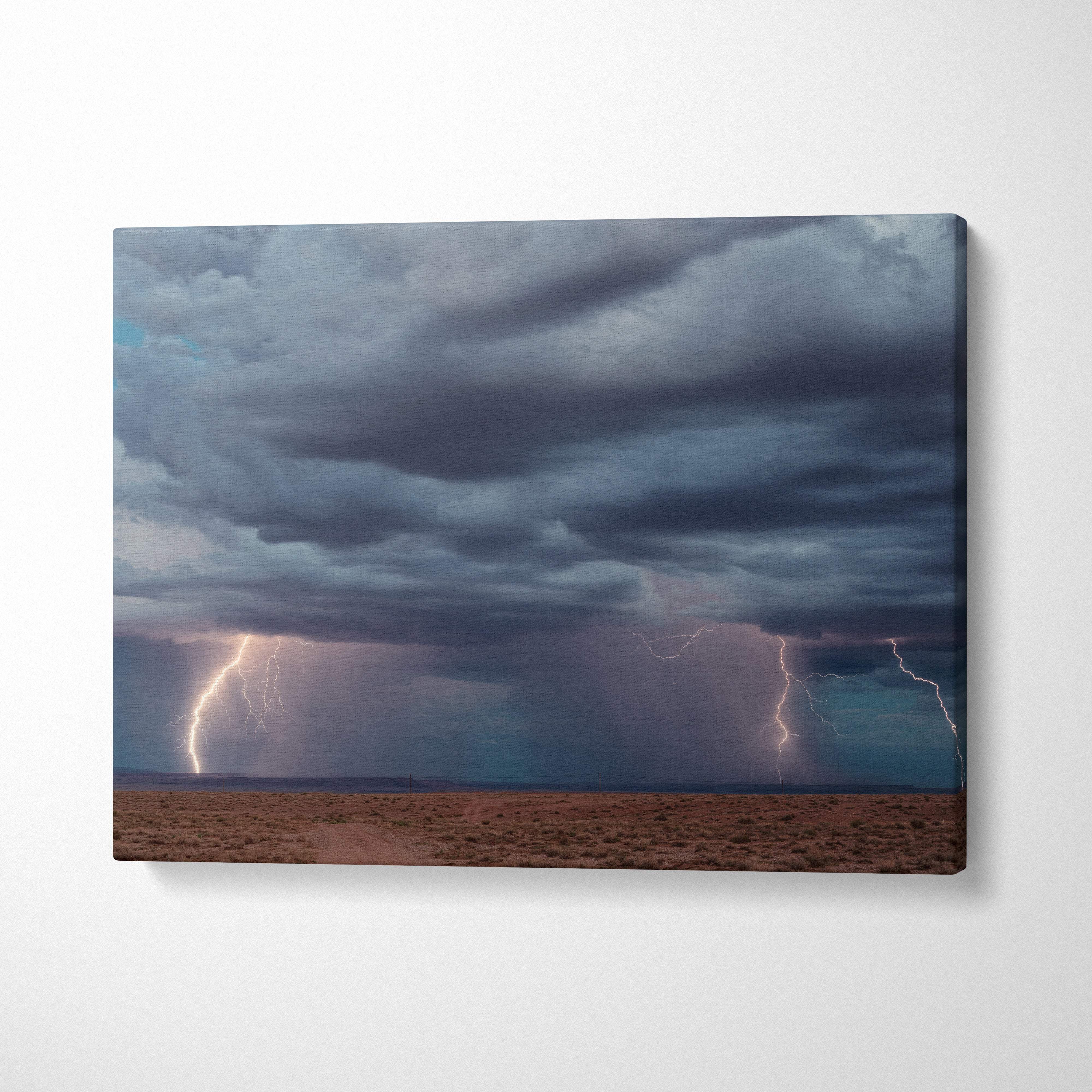 Canvas print of a dramatic desert storm with multiple lightning bolts and dark blue thunderclouds over a barren landscape