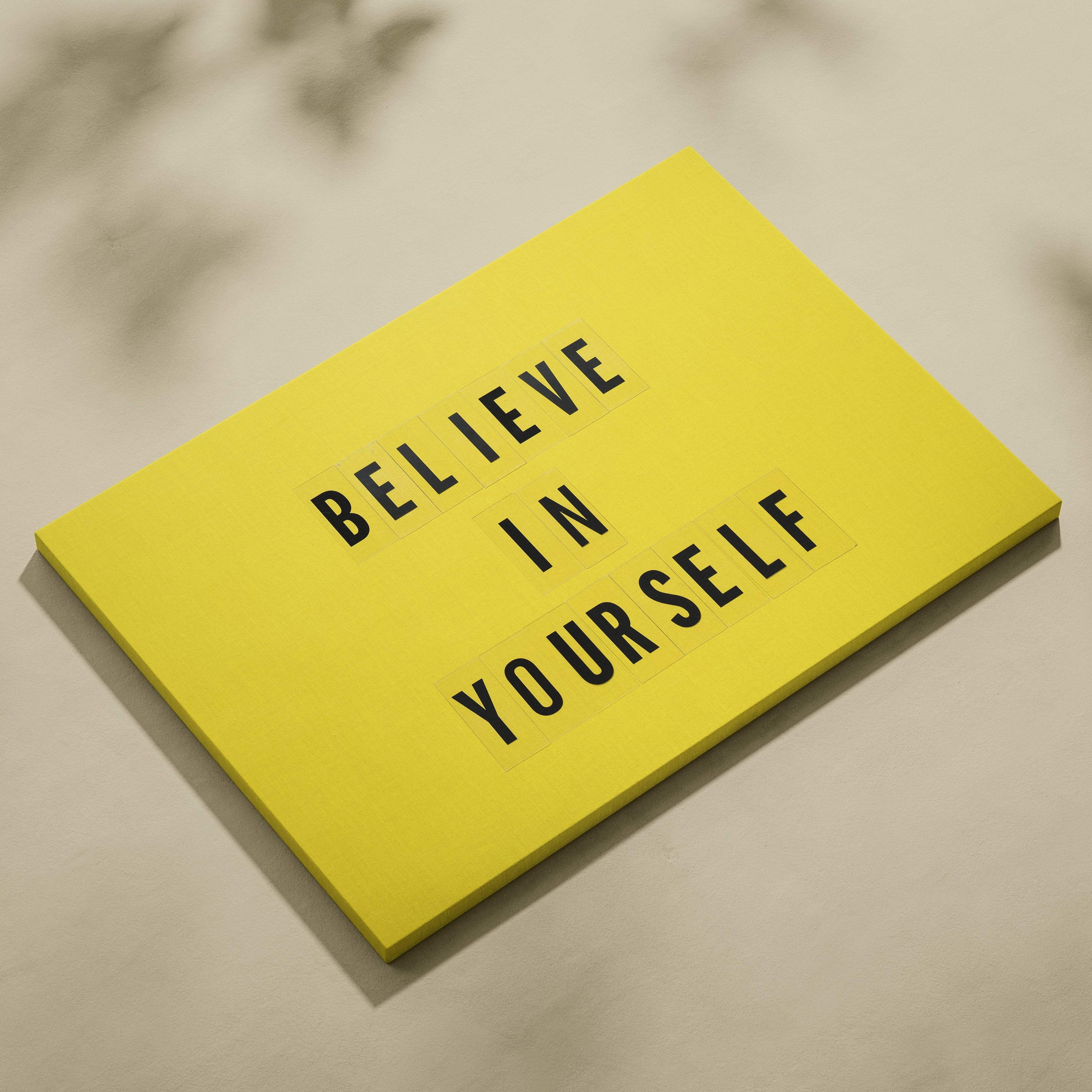 Bright yellow rectangular notepad with black letter tiles spelling believe in yourself motivational wall art print