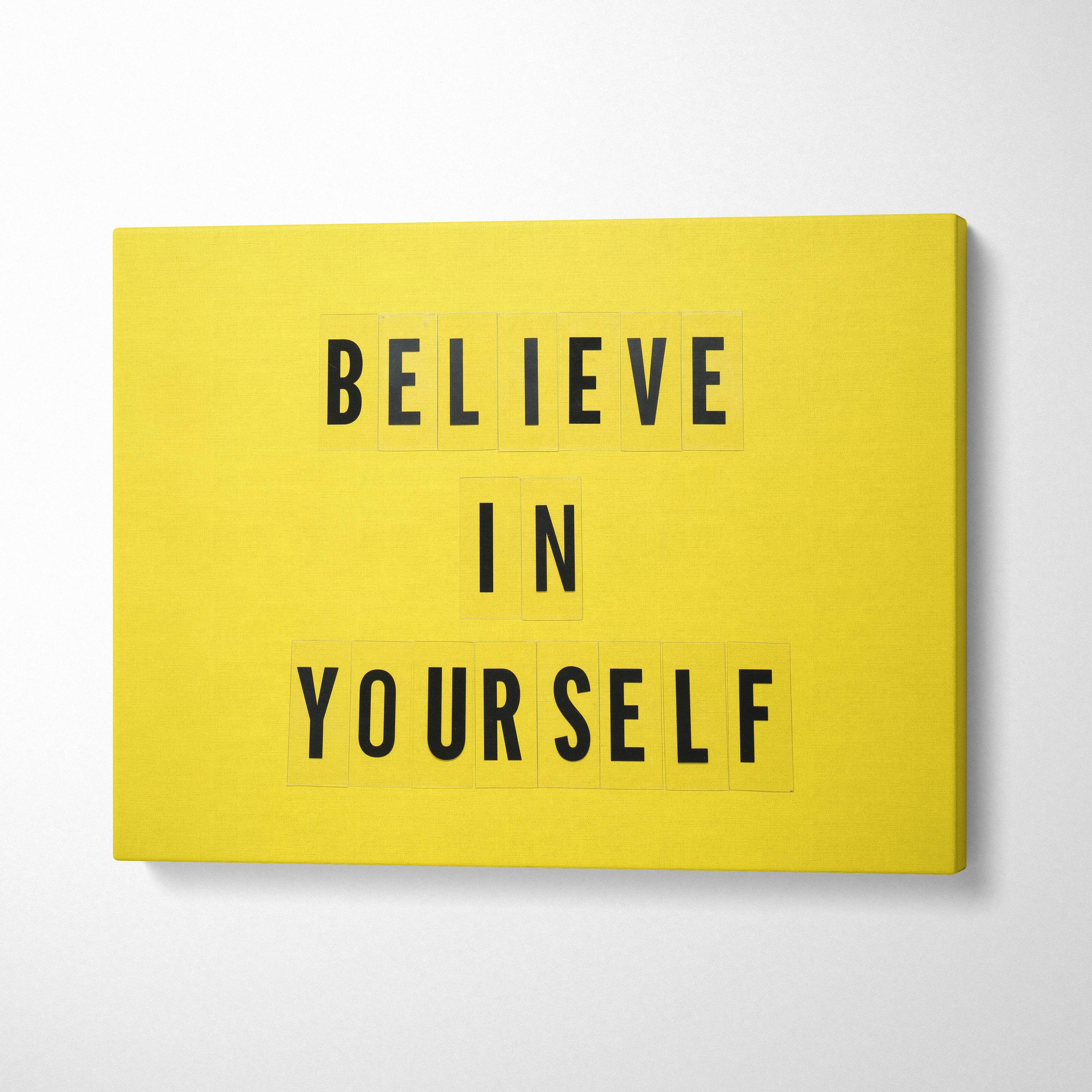 Bright yellow canvas wall art with bold black letter tiles spelling believe in yourself for office bedroom decor