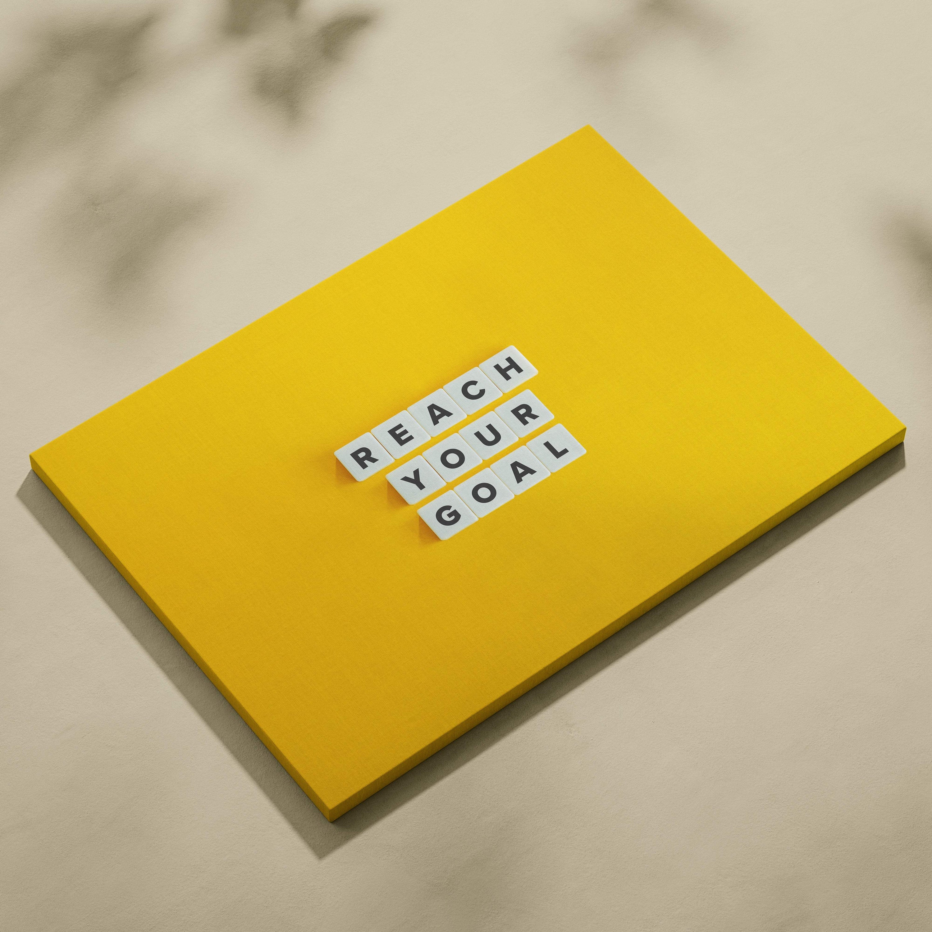Bright yellow notebook with reach your goal white letter tiles for motivational wall art print and positive decor