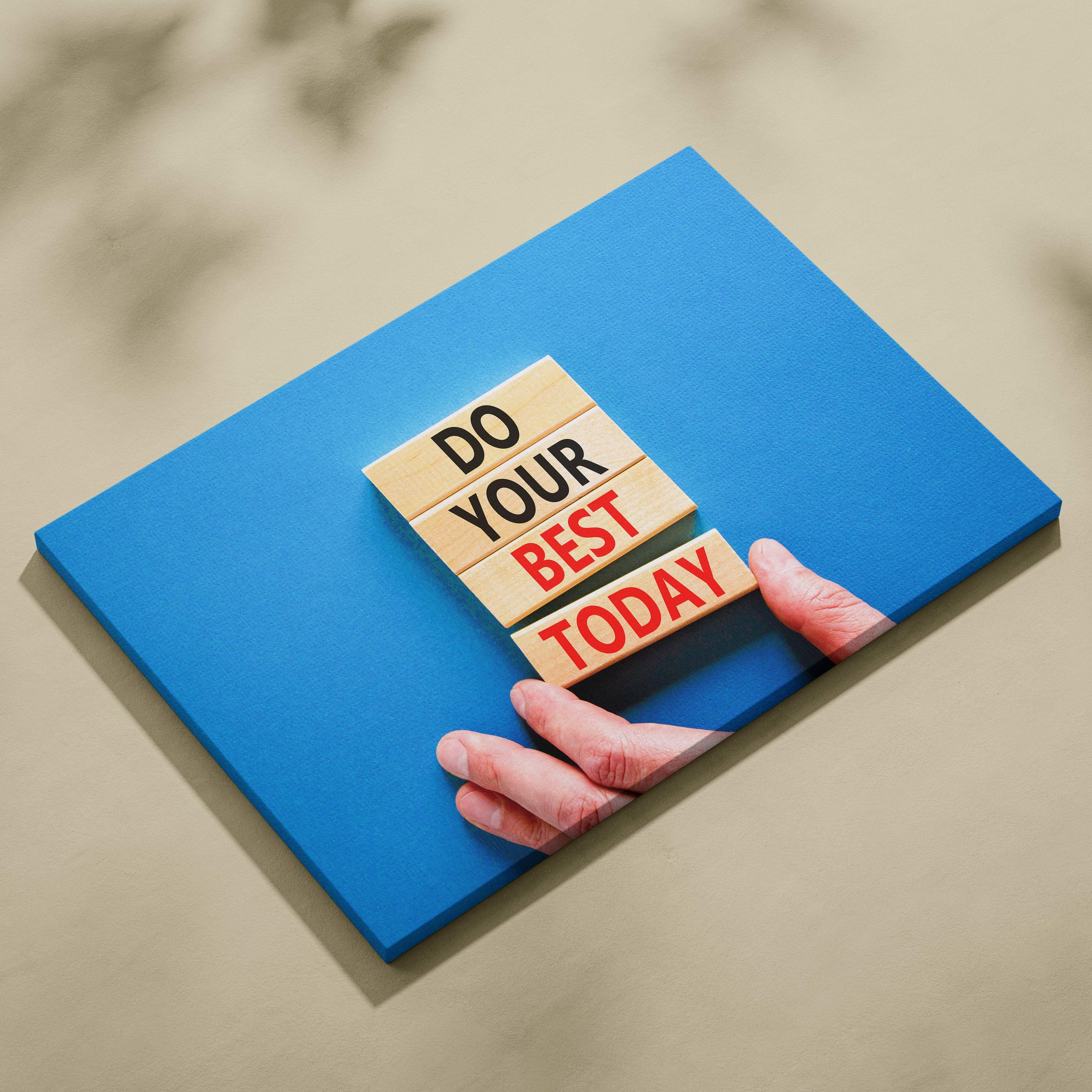 A hand gently holds four light wooden blocks with do your best today printed on a blue motivational canvas print