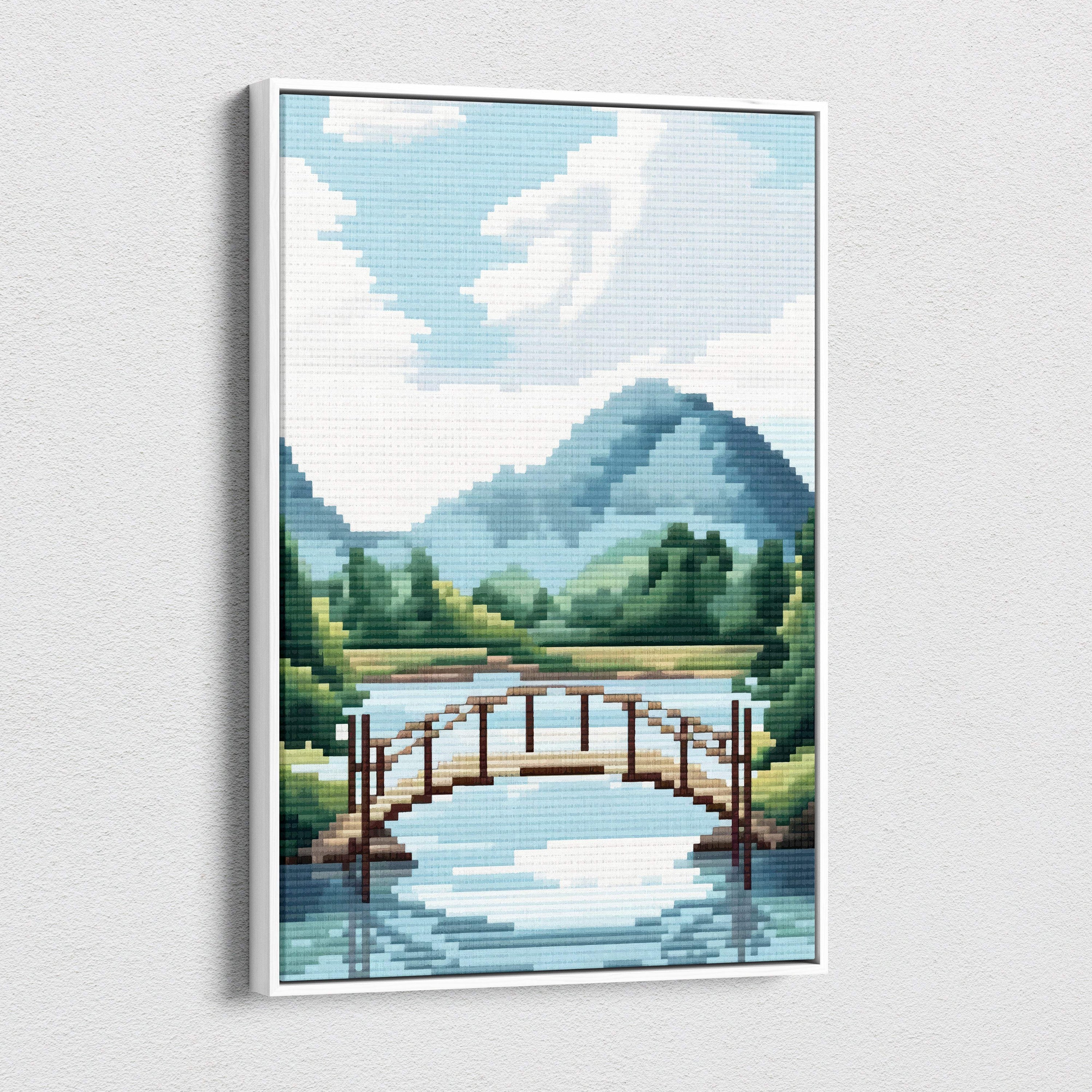 A framed pixel art canvas print of a wooden arched bridge over calm water with mountains and trees under blue sky