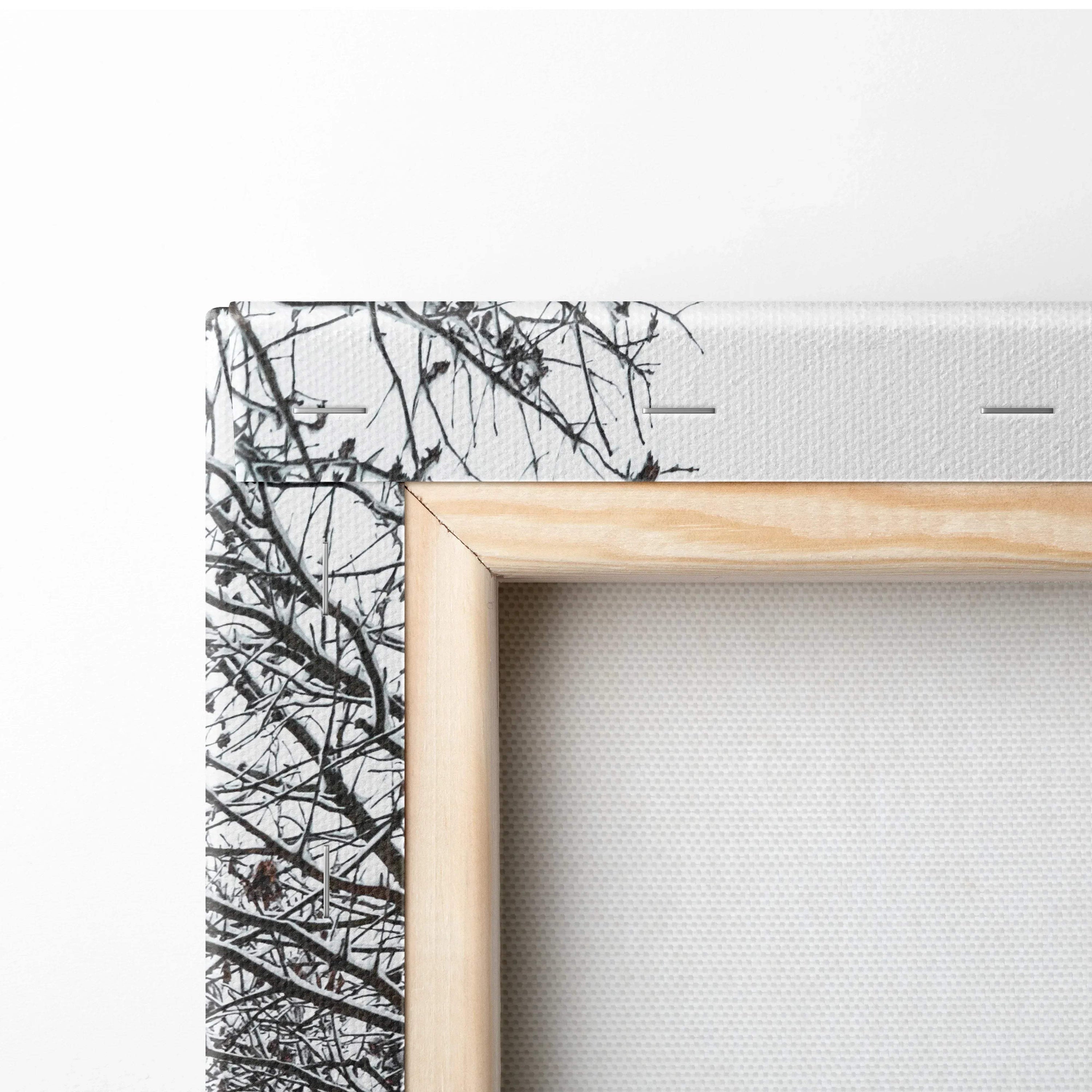 Close-up of canvas wall art corner showing snowy tree branches and natural wood frame for home decor.