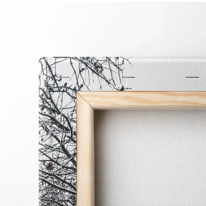 Close-up of canvas wall art corner showing snowy tree branches and natural wood frame for home decor.