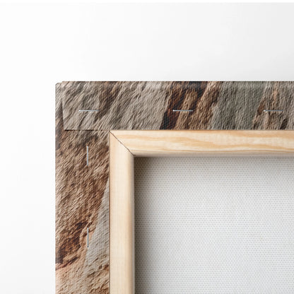 Close-up of natural wood frame corner surrounding white stretched canvas with textured beach-themed print on outer edge.