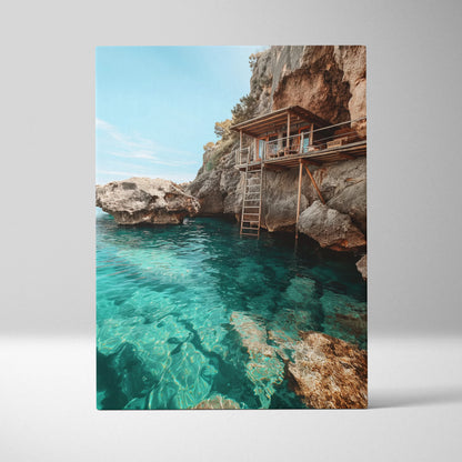 Canvas wall art depicting a rustic wooden cabin on a rocky cliff above clear turquoise beach water.