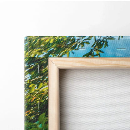 Close-up of wooden-framed canvas wall art showing vibrant green leaves and blue sky background.