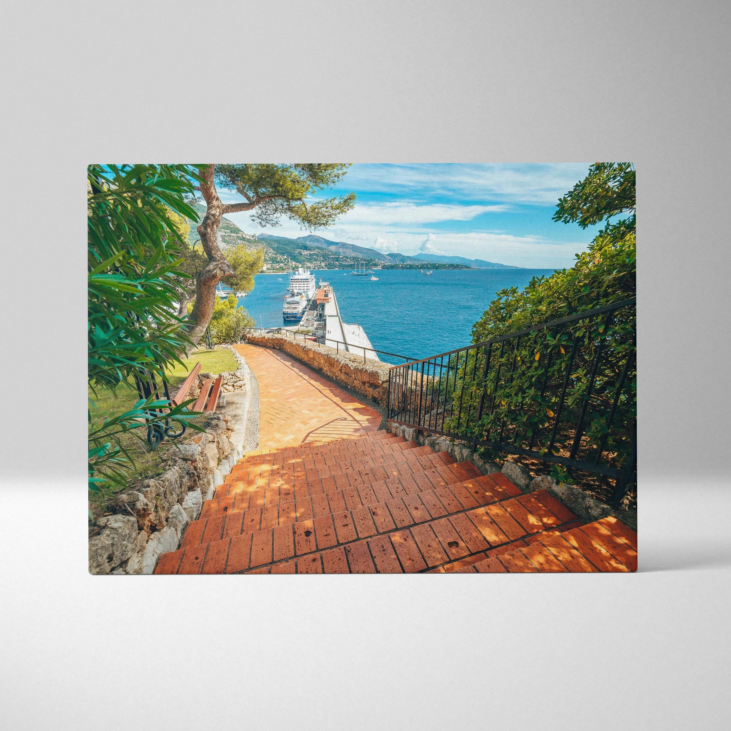 Canvas wall art featuring a sunlit brick pathway leading to a coastal building, with vibrant green trees and bright blue sky