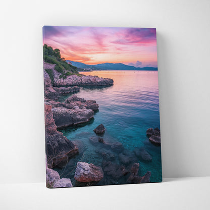 Canvas wall art depicting a rocky beach at sunset with vibrant pink, purple, and orange sky over calm blue water.