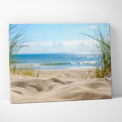 Canvas wall art featuring a sandy beach foreground with green dune grass and a calm blue ocean under a clear sky.