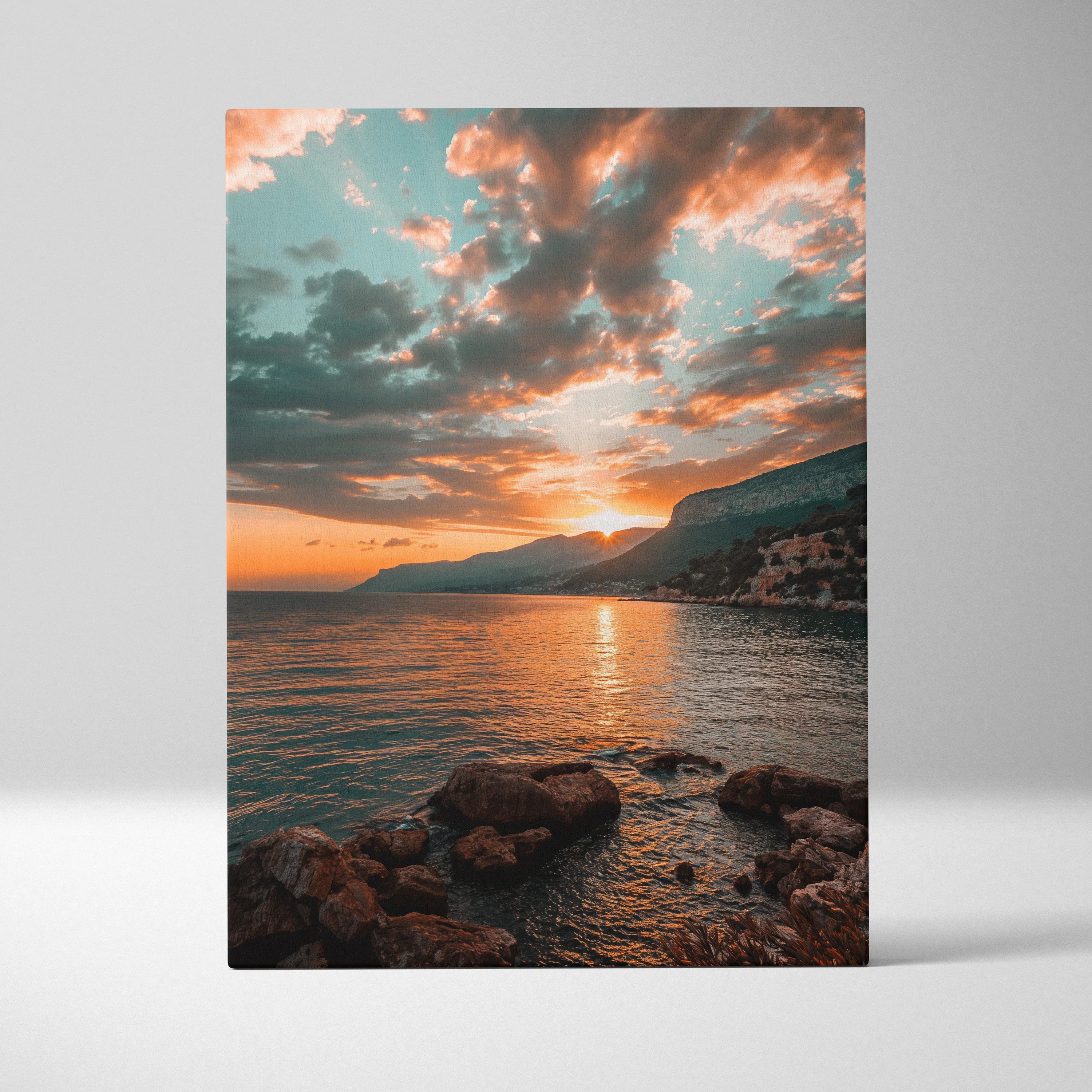 Canvas wall art showing a colorful beach sunset with orange and blue sky over calm water and rocky shoreline.