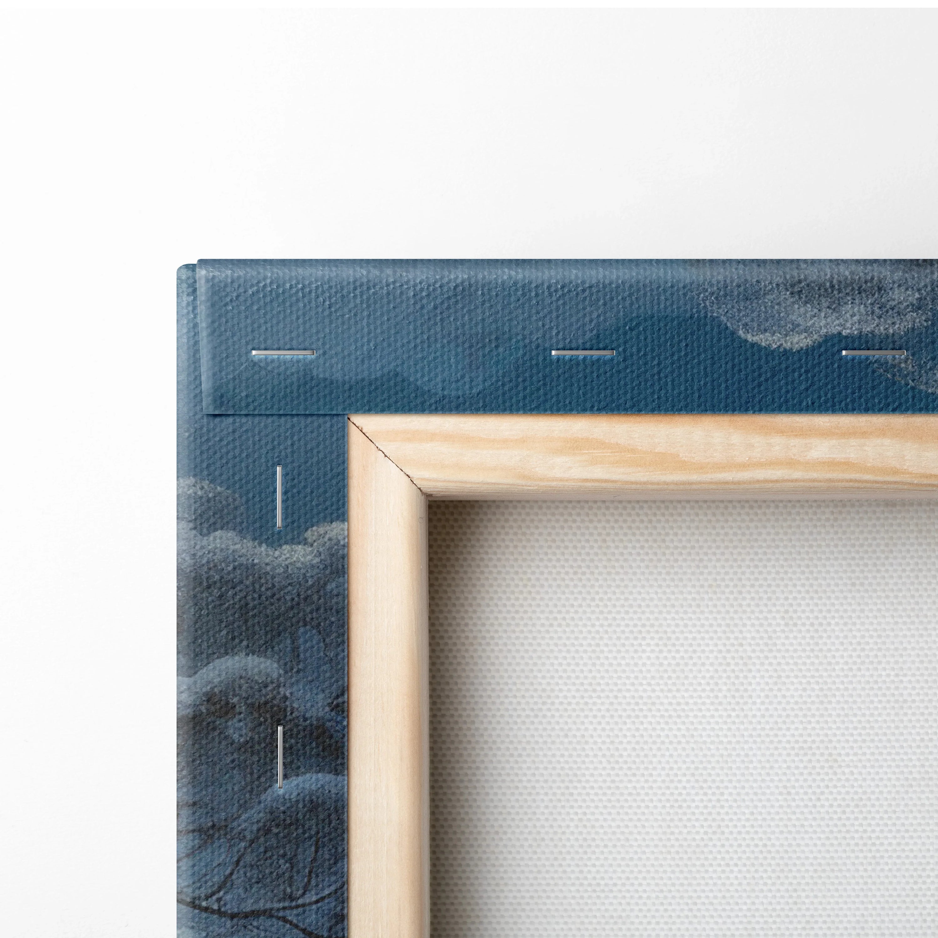 Close-up of wooden frame corner with stretched white canvas and dark blue printed edge showing snowy winter landscape.