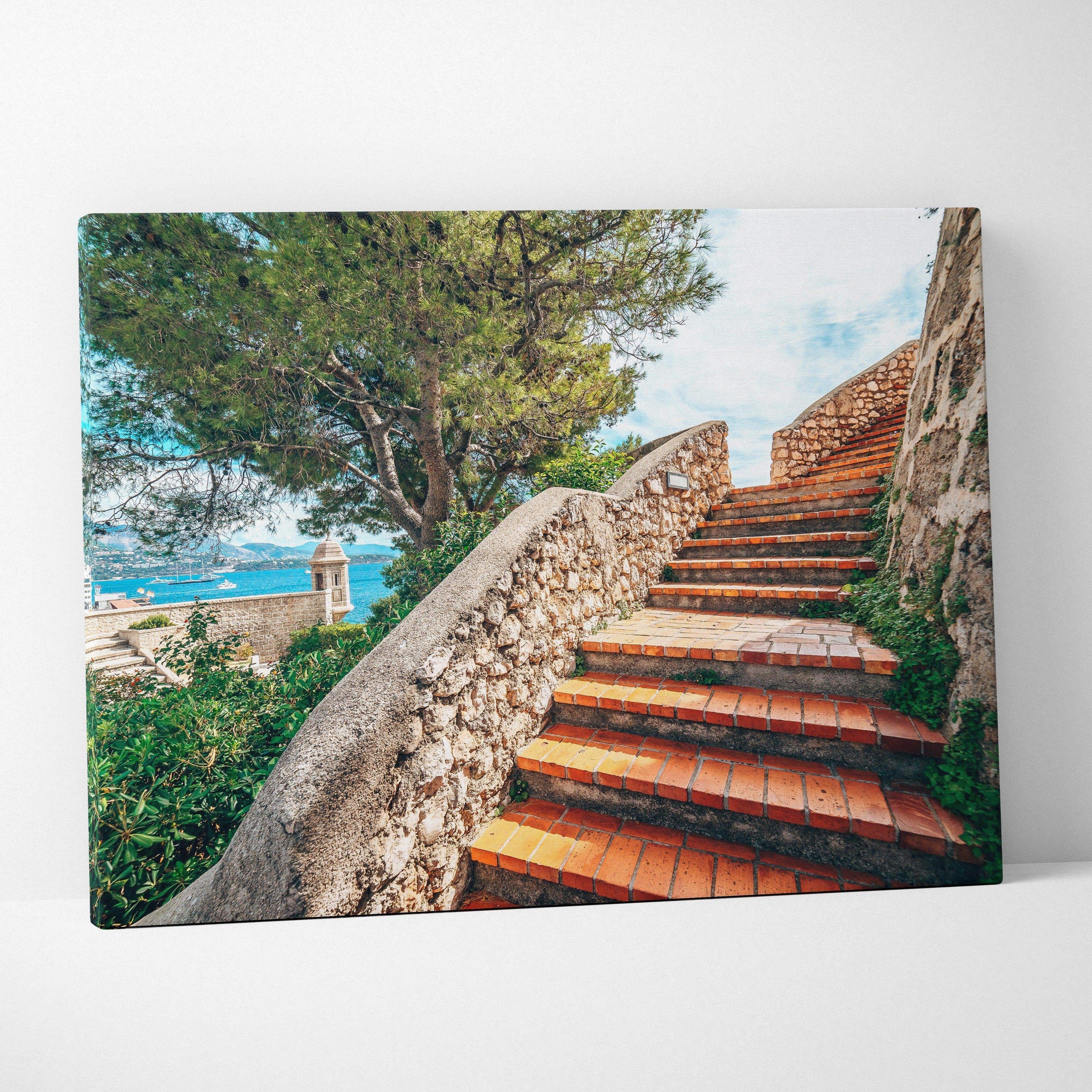 Canvas wall art featuring terracotta stone stairs winding upward beside a rustic stone railing, surrounded by green trees.