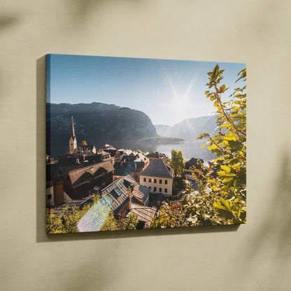 Sunlit architectural canvas wall art depicting European village with church steeple and mountains.