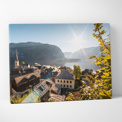 Canvas wall art featuring a sunlit European village with rustic rooftops, a church steeple, and mountains in the background.