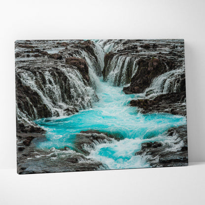 Canvas wall art depicting a turquoise waterfall flowing through dark rocky terrain with textured water details.