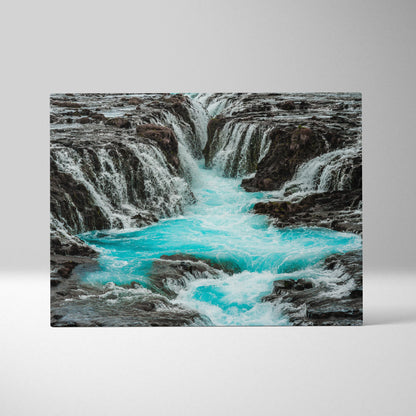 Turquoise waterfall flowing through dark rocky landscape canvas wall art decor.
