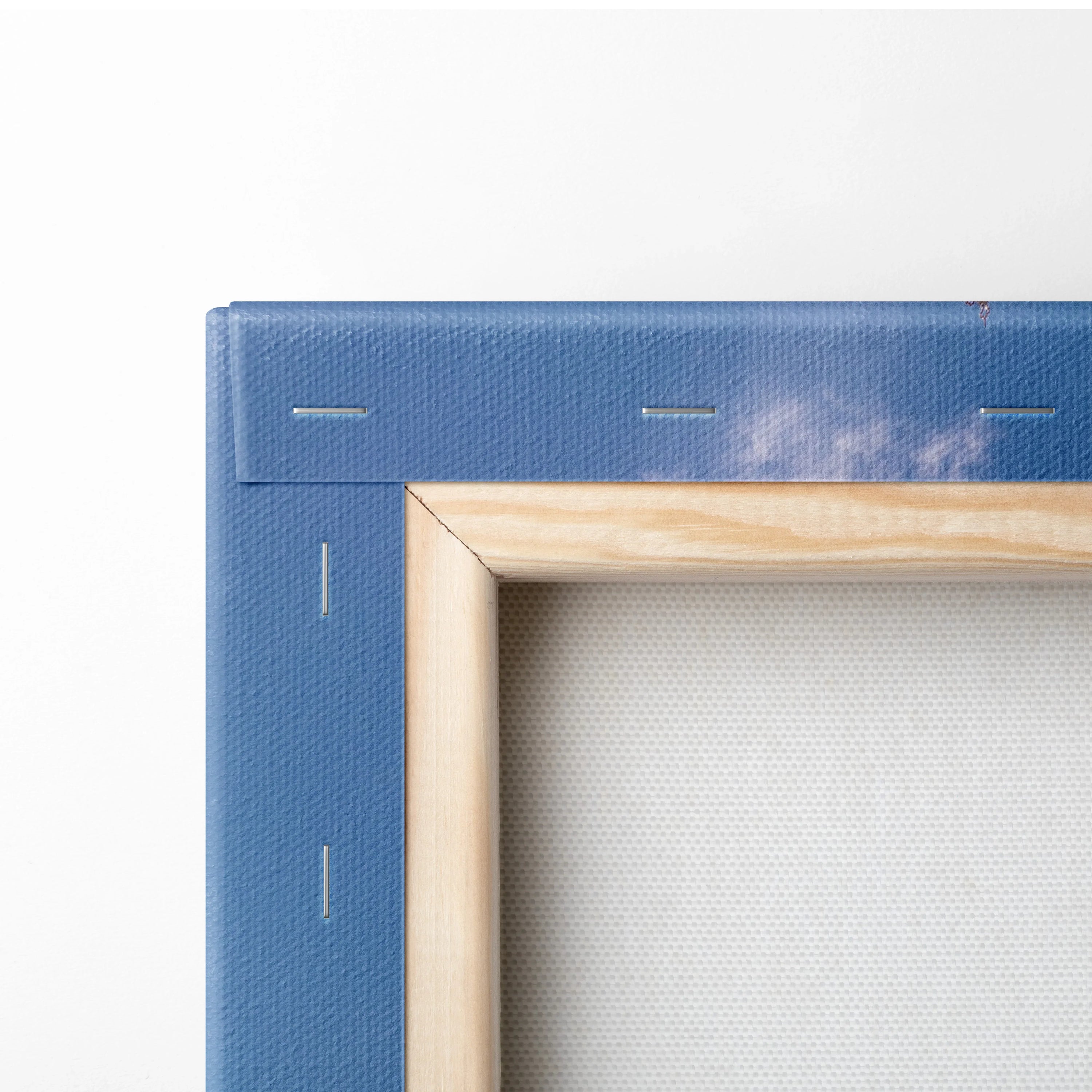 Close-up of stretched canvas on wooden frame with blue fabric backing and visible staples.