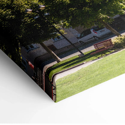 Corner of a stretched canvas print showing a city street with cars, buildings, and green park areas under trees.